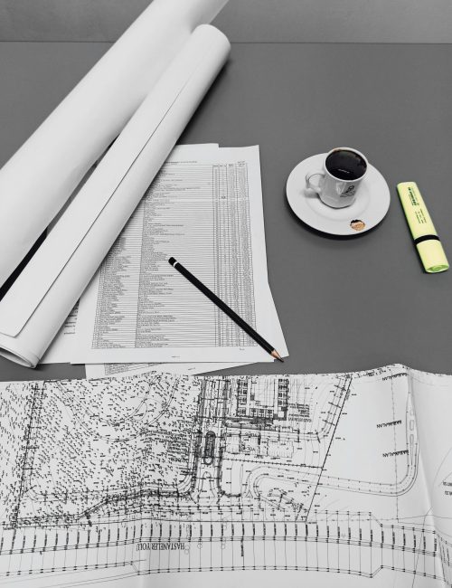 Architectural blueprints and drafts with a cup of coffee and stationery on a minimalist desk.
